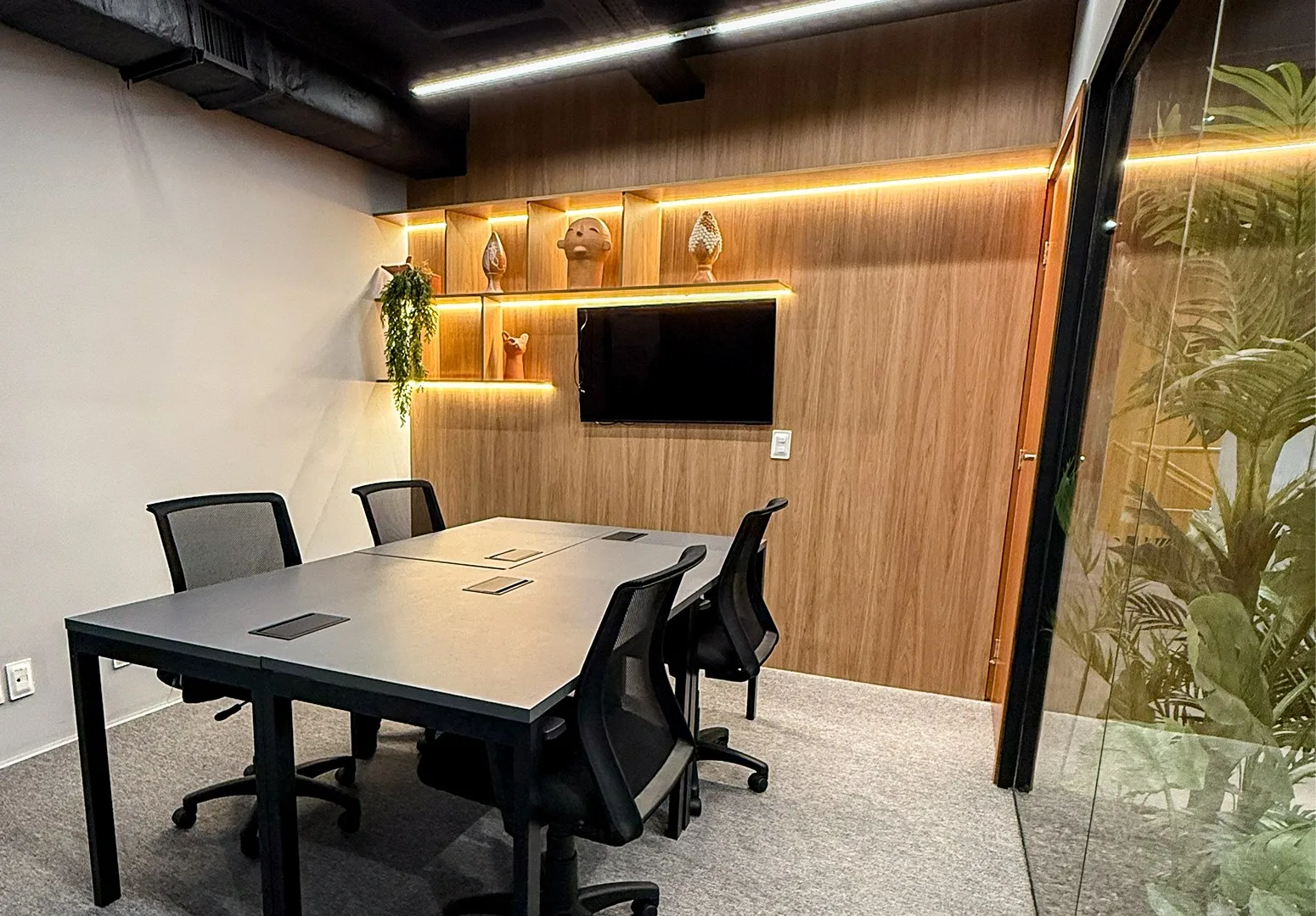 Sala de reunião para 4 pessoas com TV e marcenaria iluminada